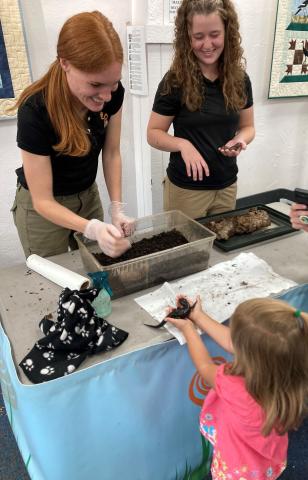Animal Wonders' staff at table with young patron holding a small creature