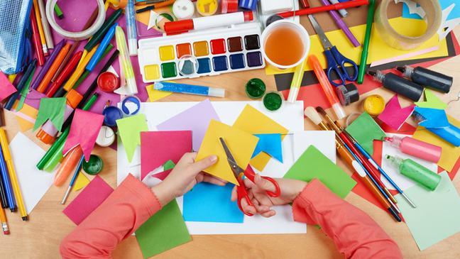 craft and art supplies and a child's arms and hands cutting a piece of paper