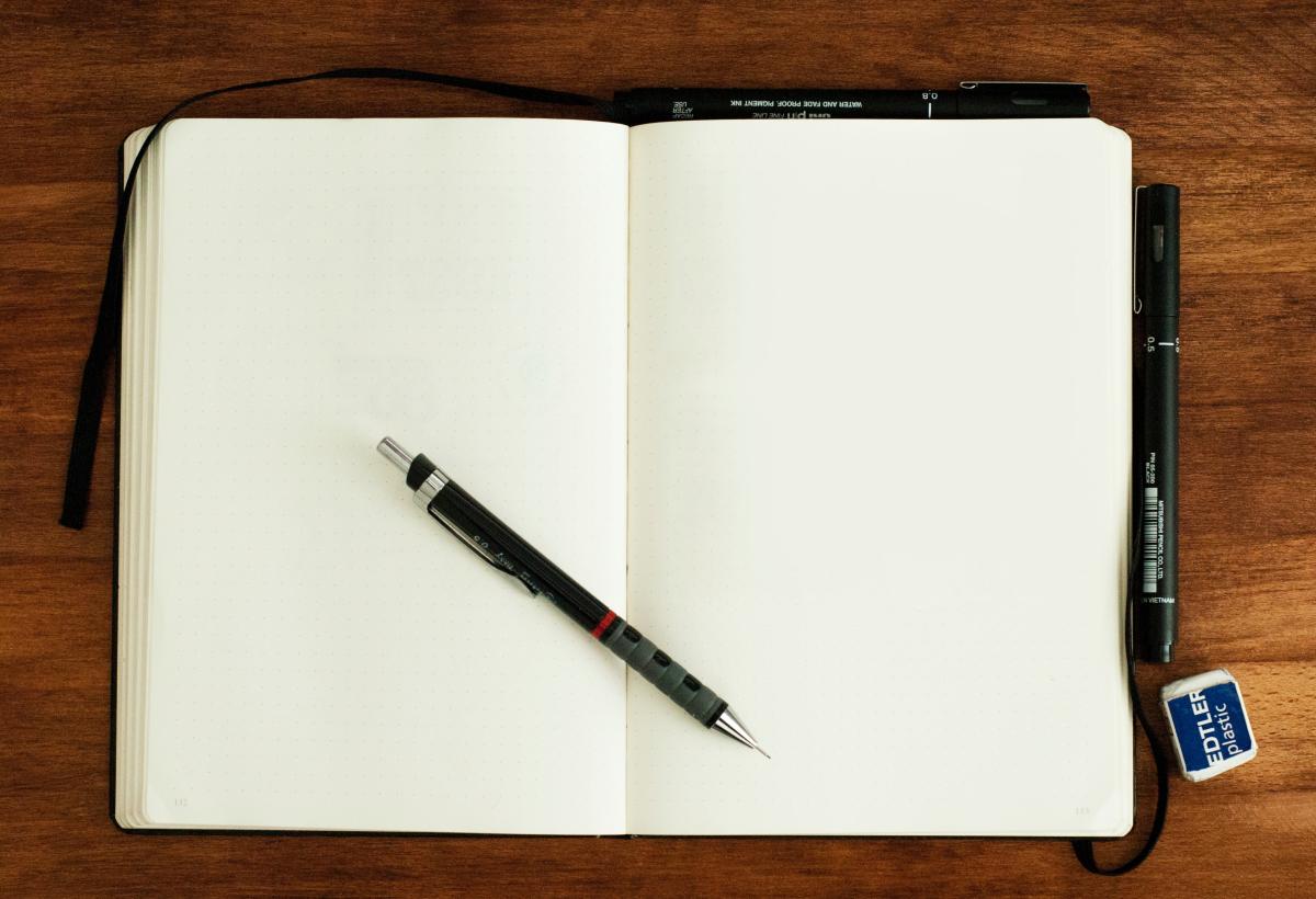 Open notebook with blank pages on a wooden desk with a fountain pen. 